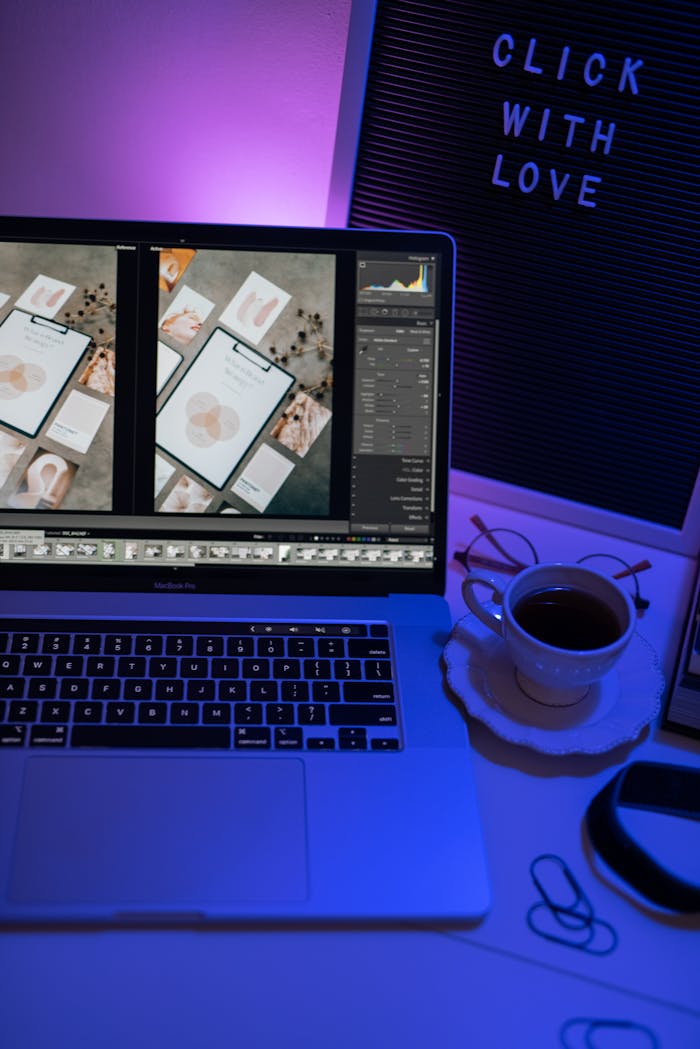 A cozy workspace setup featuring a laptop with photo editing software, lit by ambient purple light, and a cup of coffee.